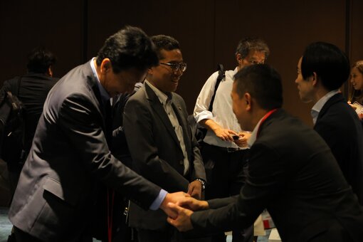 Two people shaking hands at an event with others standing nearby.