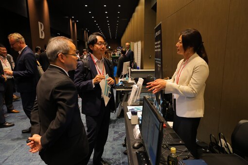 Person explaining information at an exhibition booth with brochures and monitors.