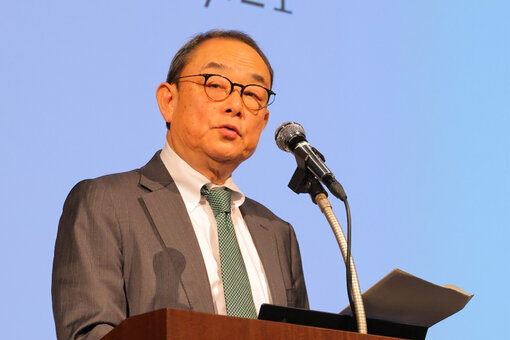 Person speaking into a microphone while holding papers during a presentation.